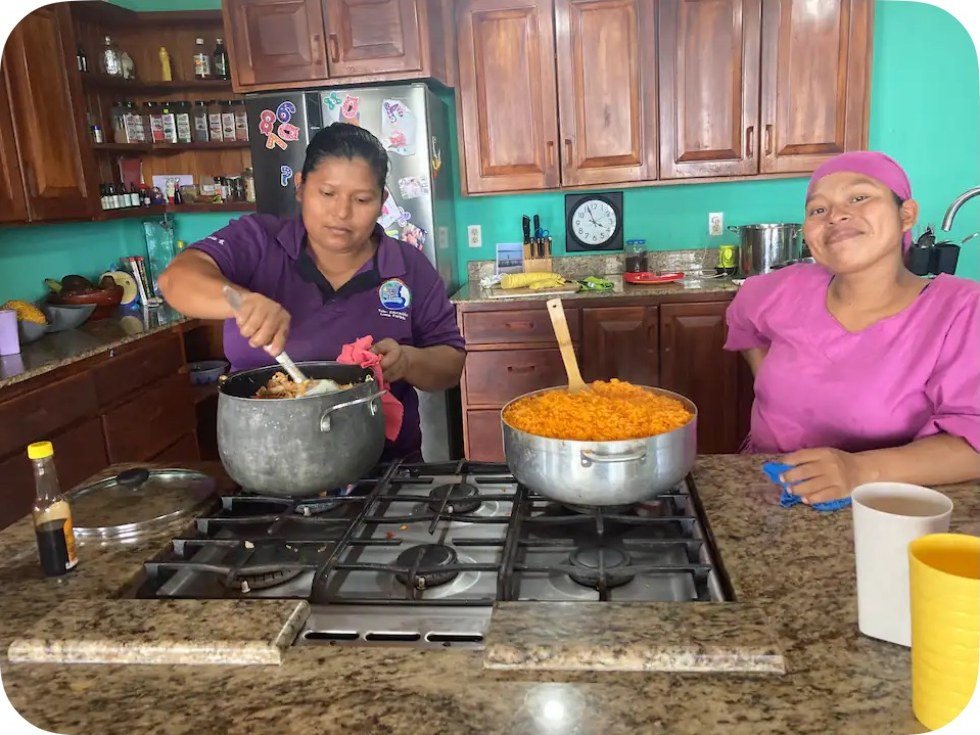 Two women from the Isla Popa community cooking together in the Toucan Bay kitchen, stirring big pots of food on the stove