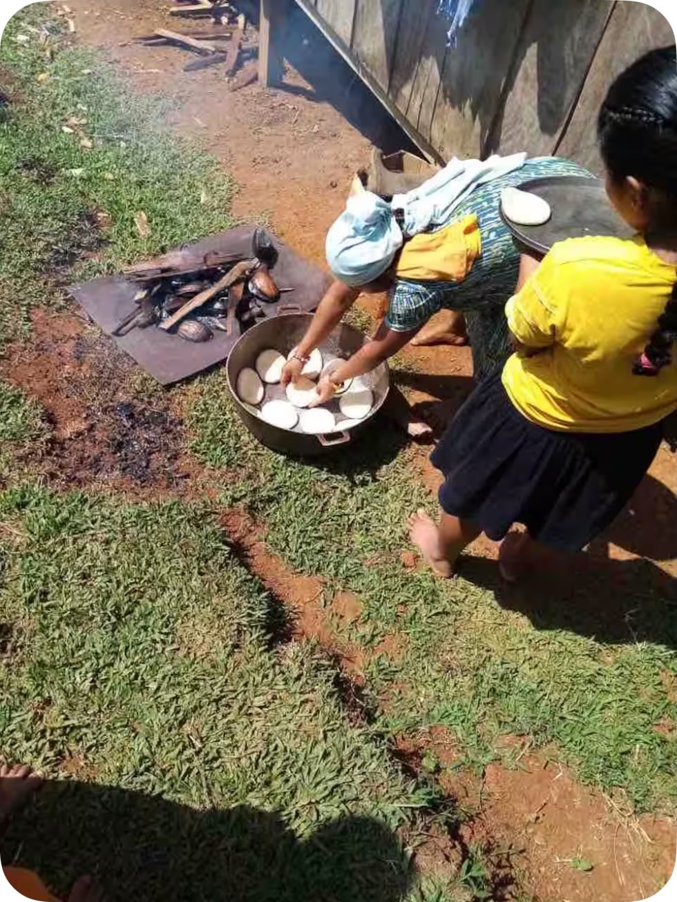 Women from the community cooking the traditional way outdoors — shaping tortillas by hand beside a wood fire